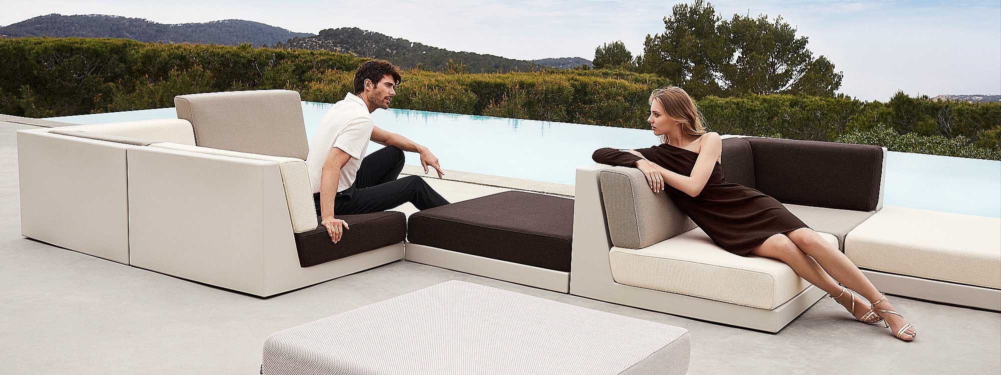Image of man and woman sat in opposing directions turned talking to one another on Vondom minimalist garden sofa