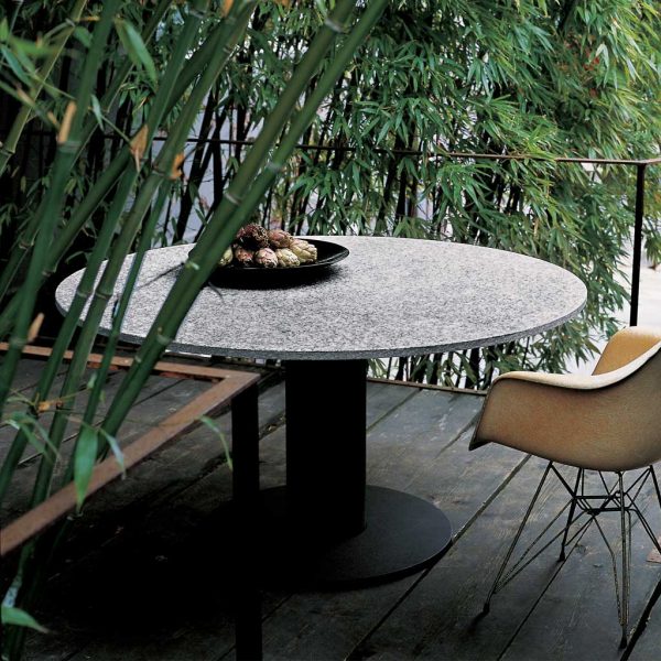 Image of RODA Platter circular garden table with smoke-colored base and grey stone top, on wooden decking in amongst bamboos