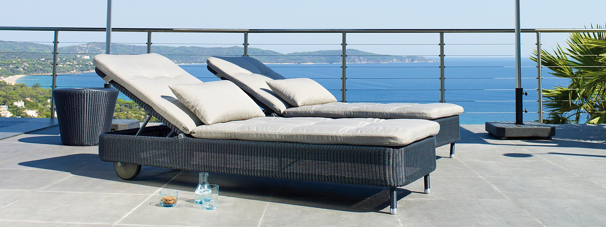Image of pair of graphite rattan Presley sun loungers by Cane-line, on terrace overlooking sea