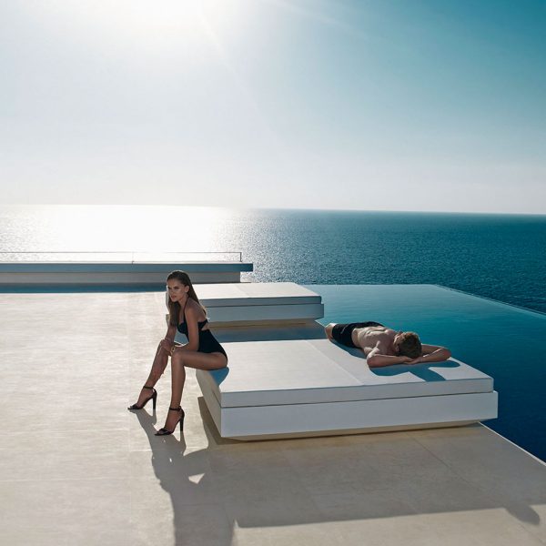 Image of couple resting on Vondom Vela minimalist outdoor daybed next to horizon swimming pool with twinkling sea in the background