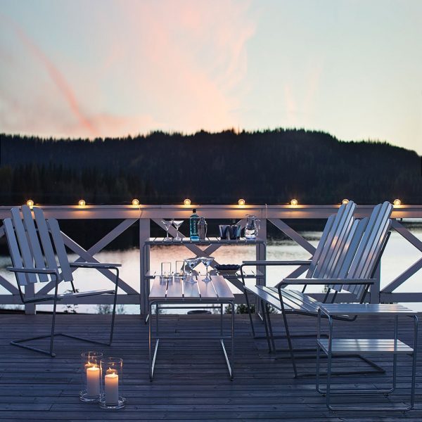 Image of Grythyttan A3 outdoor lounge chairs with galvanised steel frames and white lacquered oak surfaces, shown on lakeside decking at dusk