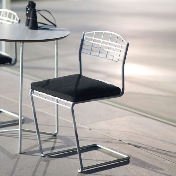 Image of Grythyttan Stålmöbler High Tech galvanised steel cantilever chair with black cushion seat pad on sunny terrace