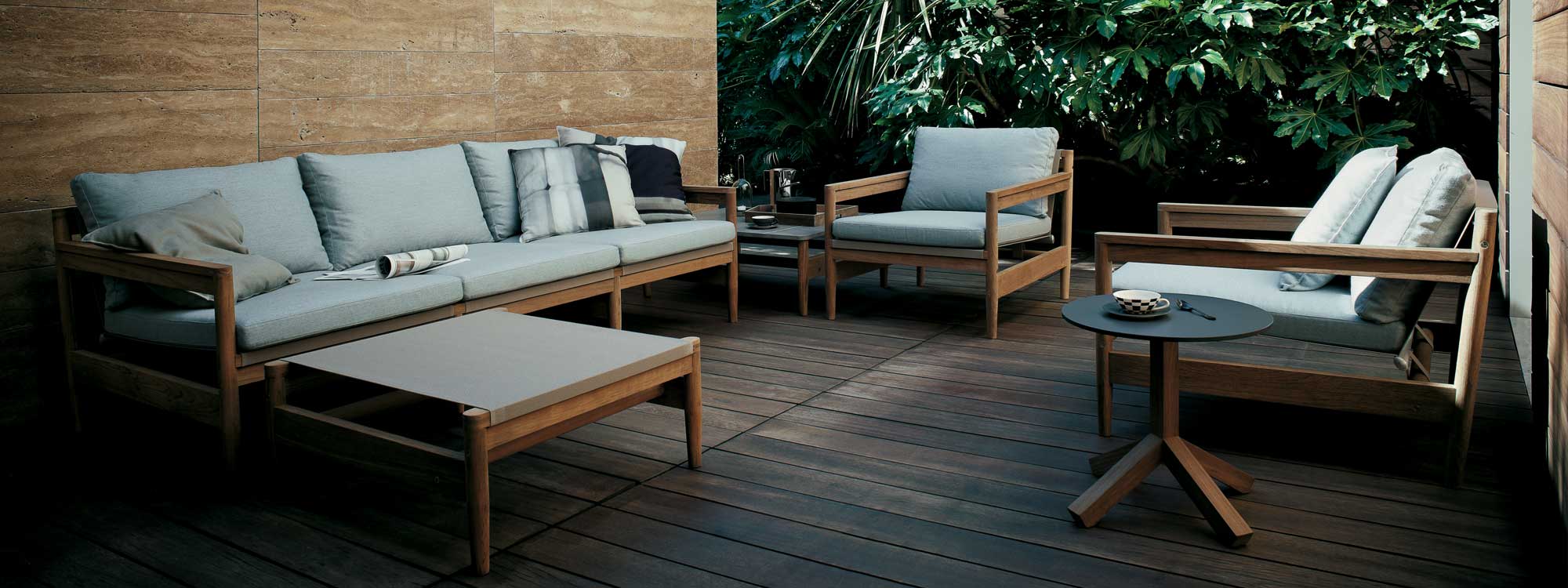 Road teak garden sofas on wooden decking with architectural planting in the background