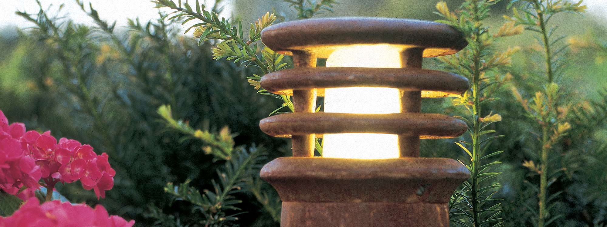 Image of Royal Botania Rusty modern garden bollard light in oxidised iron, shown with Taxus baccata in the background