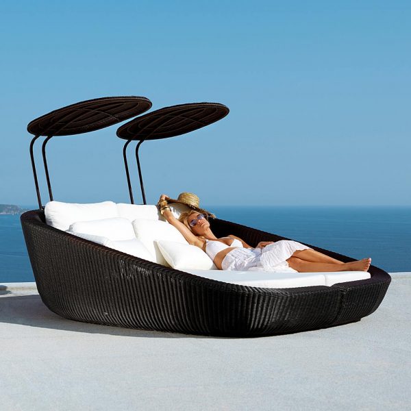 Image of woman stretching out in Savannah twin outdoor daybed in black Cane-line weave with white cushions