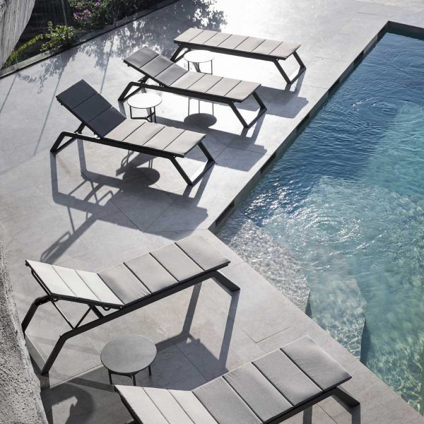 Image of Siesta aluminium sun loungers and Twist side tables by Caneline, shown around swimming pool at sunset