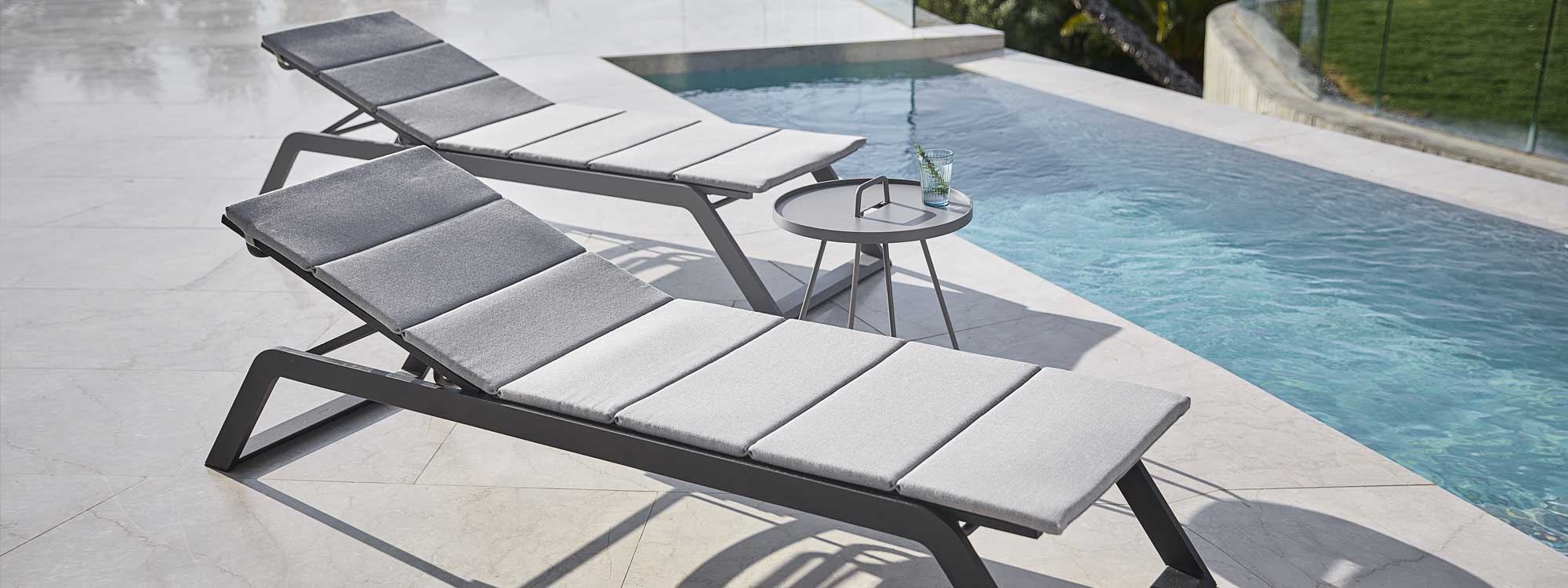 Image of pair of grey Rest sun loungers and On The Move tray table by Cane-line shown on poolside