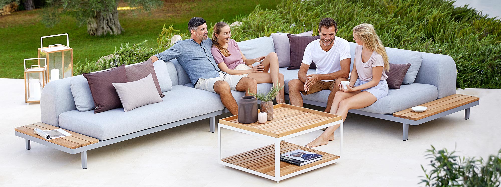 Image of 2 couples sat on Space modern corner sofa in light grey with Level teak low table in centre, by Cane-line