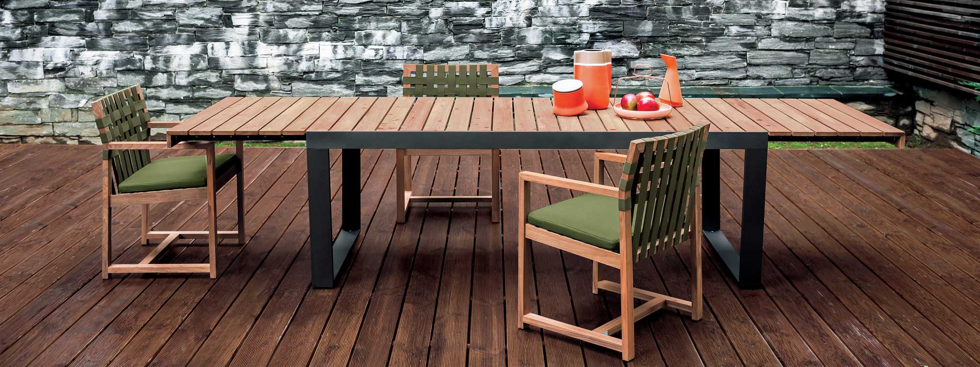 Image of RODA Spinnaker extendable garden table with dark grey frame and teak top, together with Network teak outdoor chairs with green webbing and green cushions