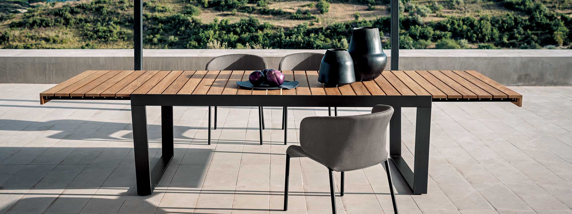 Image of RODA Spinnaker 12 seat extending garden table with Double chairs, shown on sleek terrace with countryside in the background