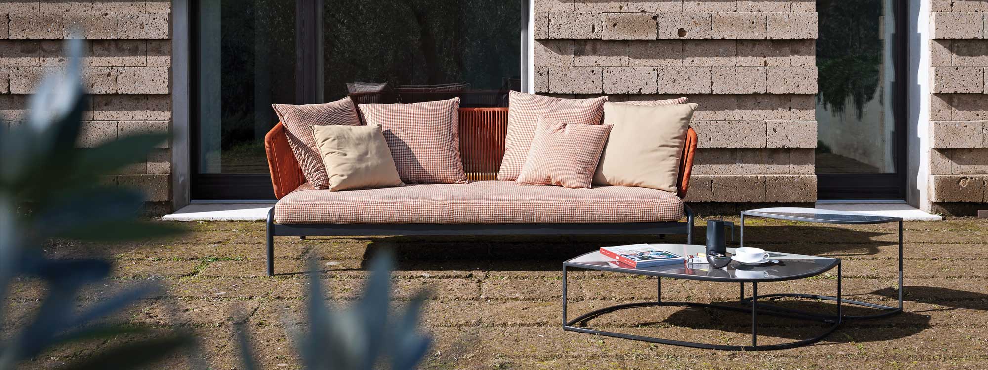 Image of RODA Spool orange garden sofa with white and orange cushions, together with Leaf minimalist outdoor low tables on sunny terrace