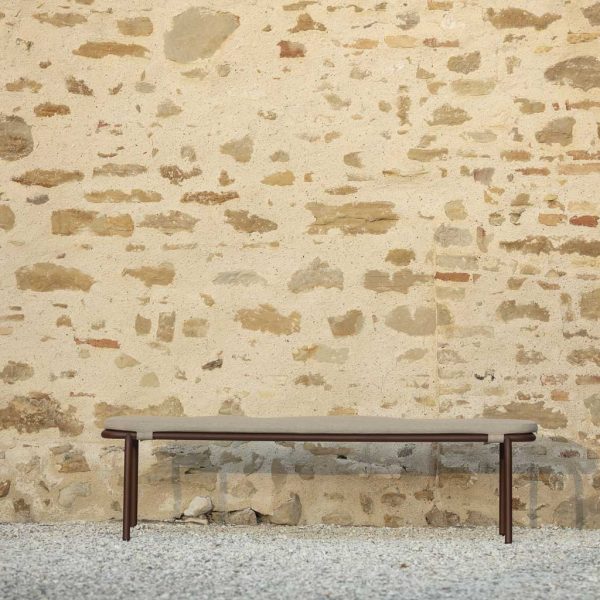 Image of Todus Starling stainless steel garden bench against rustic stone wall