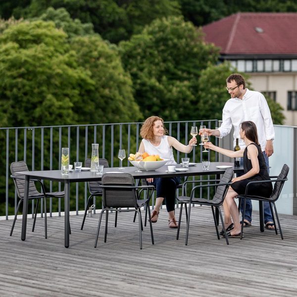 Image of adults making a toast sat and stood around Todus Starling modern garden table and outdoor chairs on rooftop terrace with trees and rooftops in the background