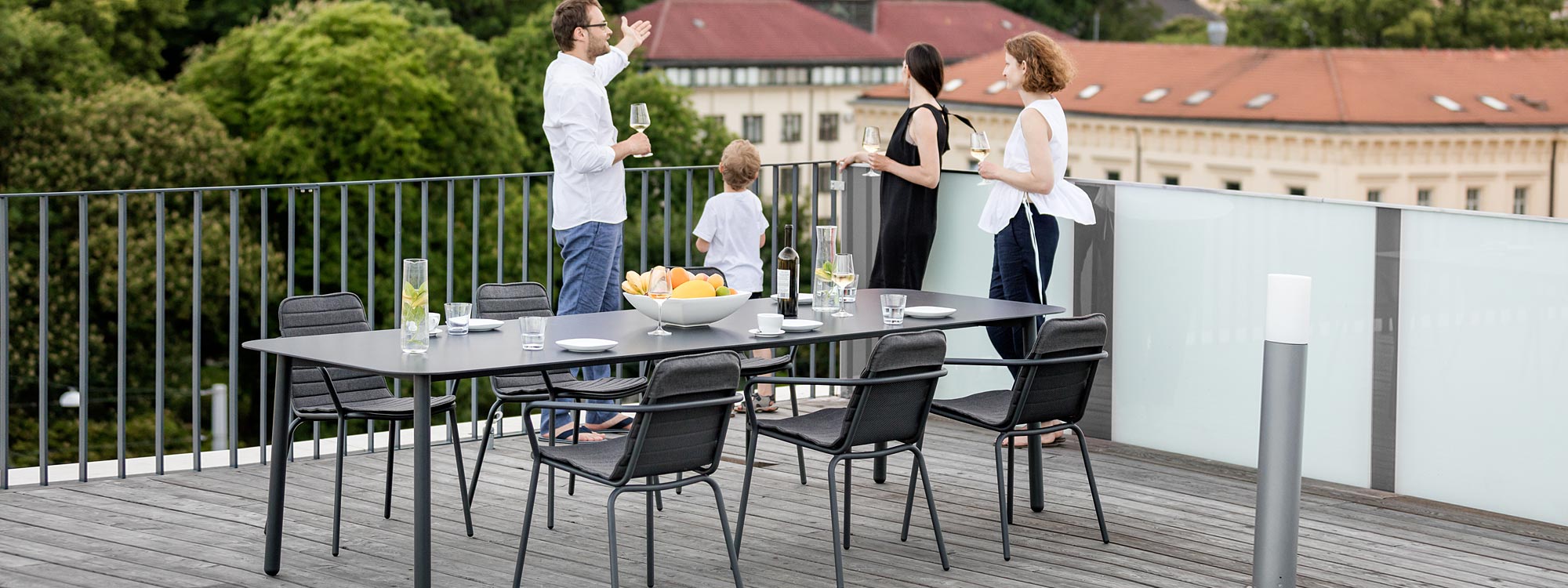 Image of adults and children on rooftop terrace at dusk, next to Starling modern garden table and outdoor chairs