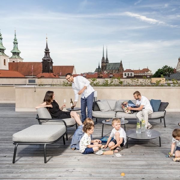 Image of adults and kids relaxing and playing on and around Todus Starling garden sofas on rooftop terrace with rooftops, church spires and steeples in the background