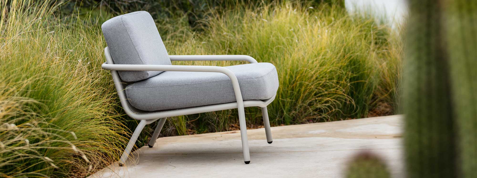 Image of Todus Starling white garden lounge chair with light grey cushions, on terrace surrounded by architectural grasses