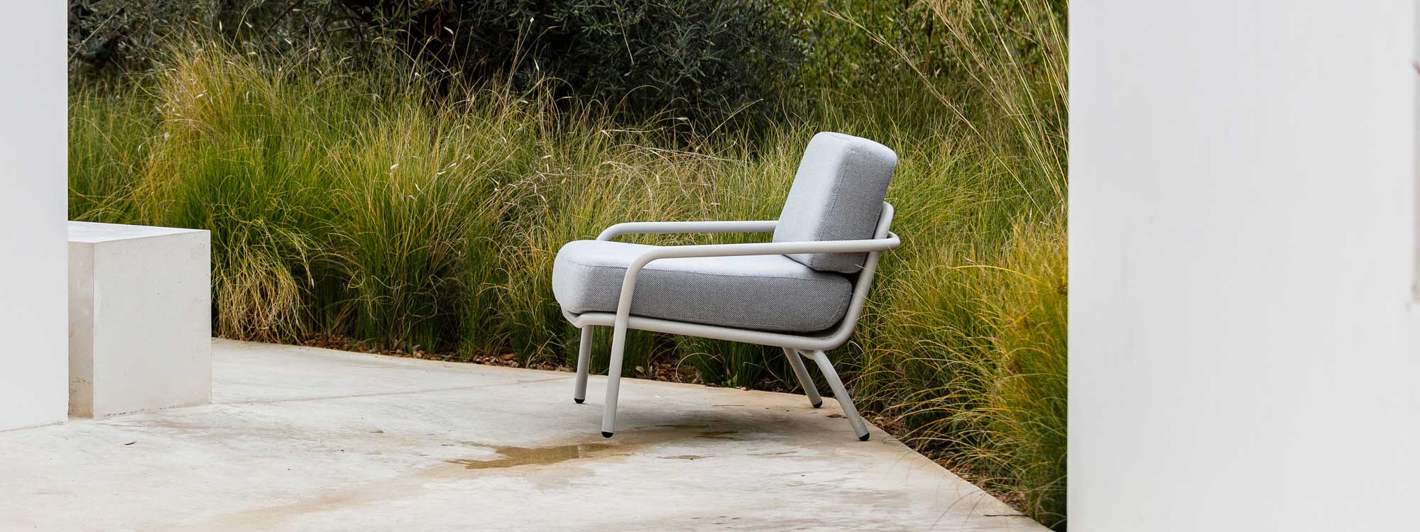 White Starling modern outdoor relax chair with White frame and Grey cushions in front of ornamental grasses