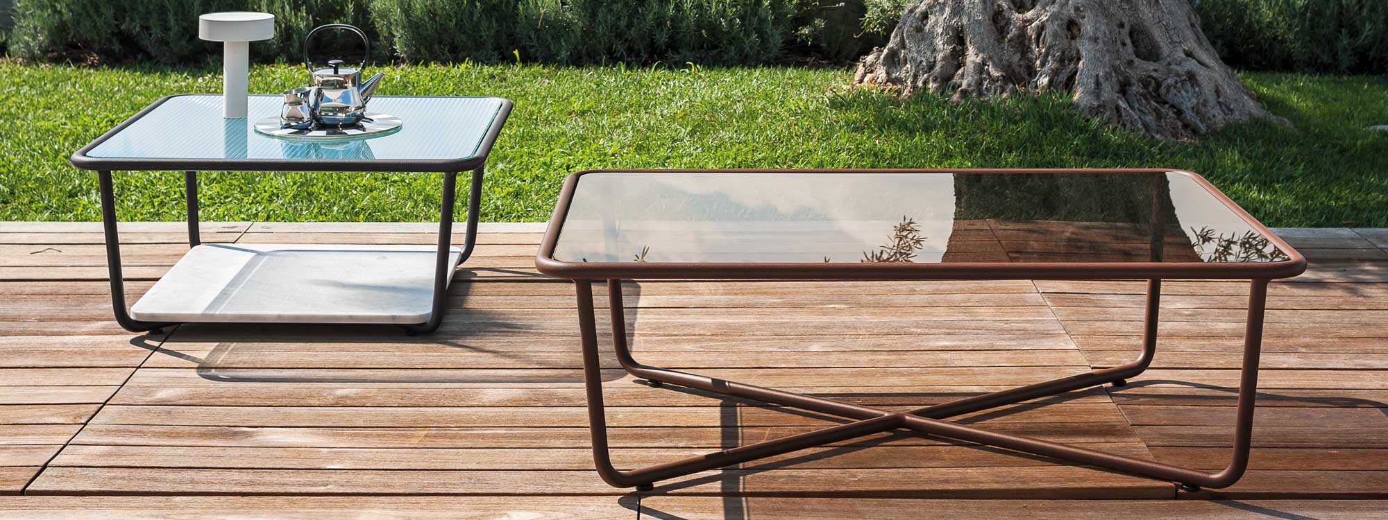 Pair of Sunglass retro low tables on wooden decking in front of olive tree trunk.