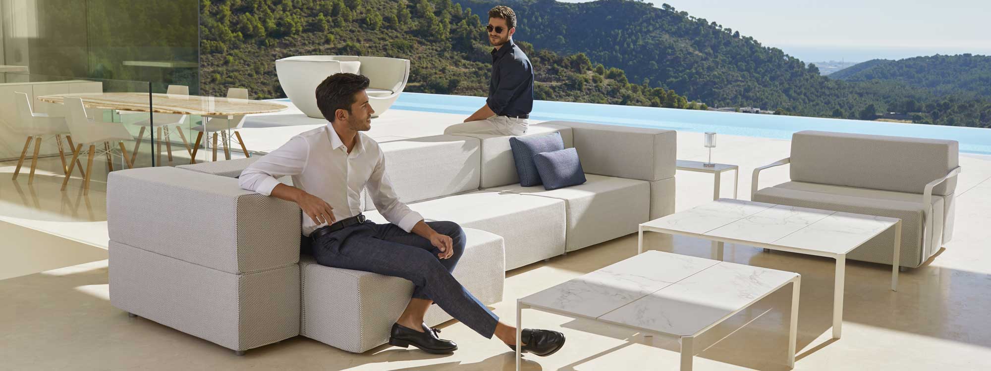 Image of couple of men sat on Vondom Tablet modern white garden sofa on sunny terrace with swimming pool and hills in the background
