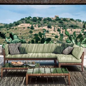 Image of RODA Teka modern teak corner sofa with light green cushions, with cactuses and arid Italian countryside in the background