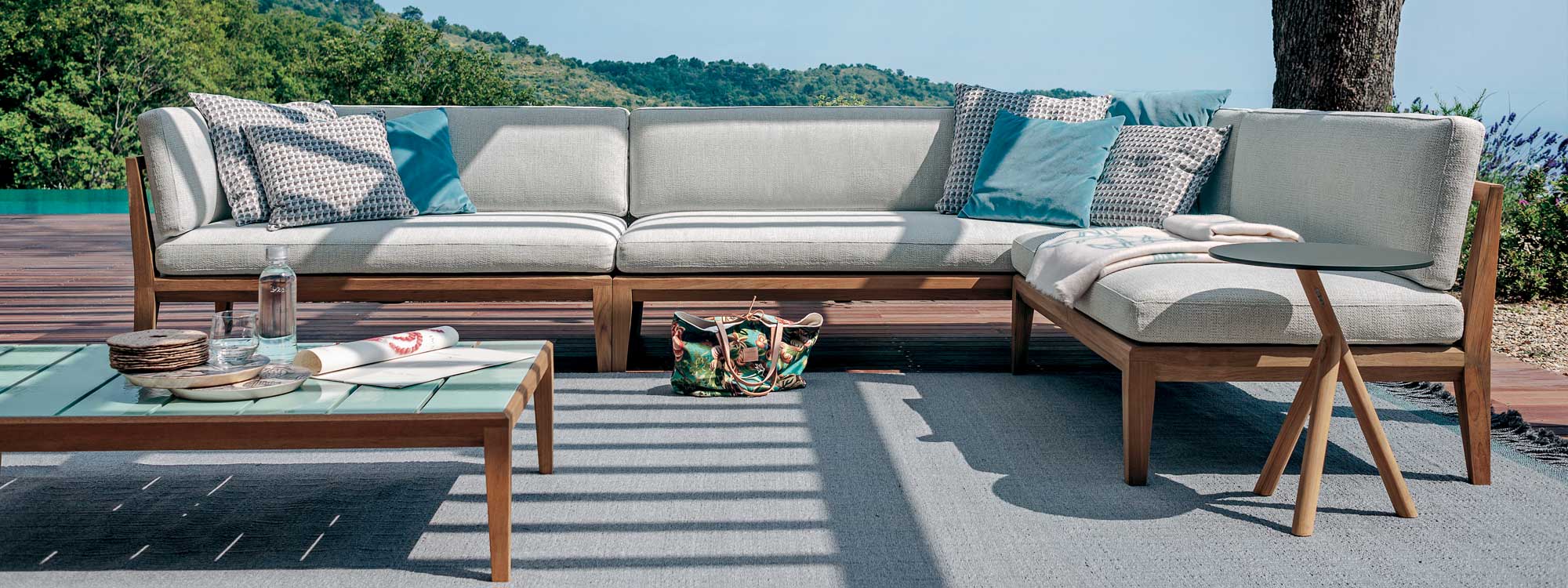 Image of RODA Teka teak garden corner sofa with heavy-knit white cushions, with Teka glazed ceramic low table and Root teak side table