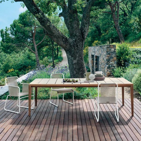 Image of RODA Teka rectangular garden table with Harp white garden chairs on decking, with trees and lavender in background