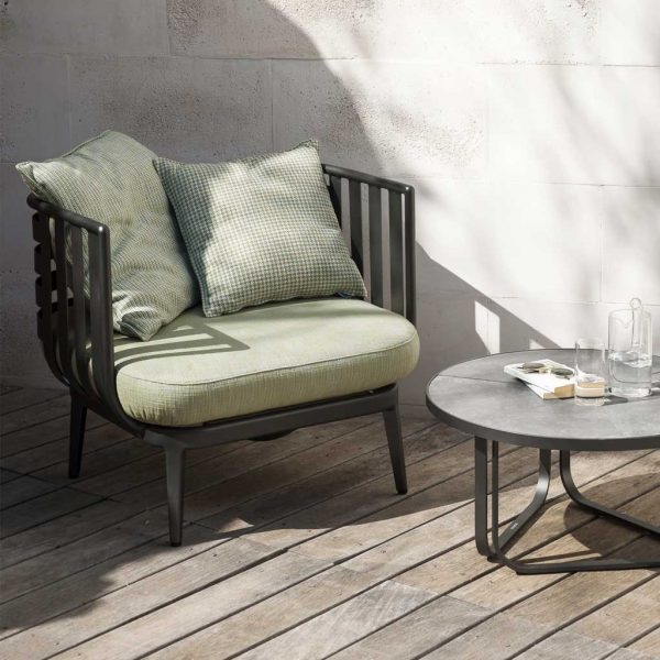 Image in sun and shade of RODA Thea exterior lounge chair and round low table, shown on decking