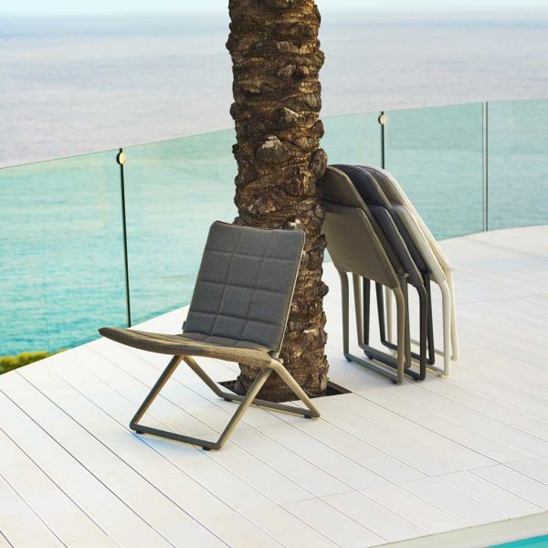 Image of Traveller outdoor lounge chairs by Caneline, folded up, leaning against a tree trunk