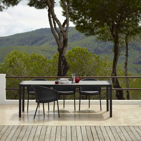 Image of Trinity black garden chairs and dining table by Caneline, with undulating hills in background