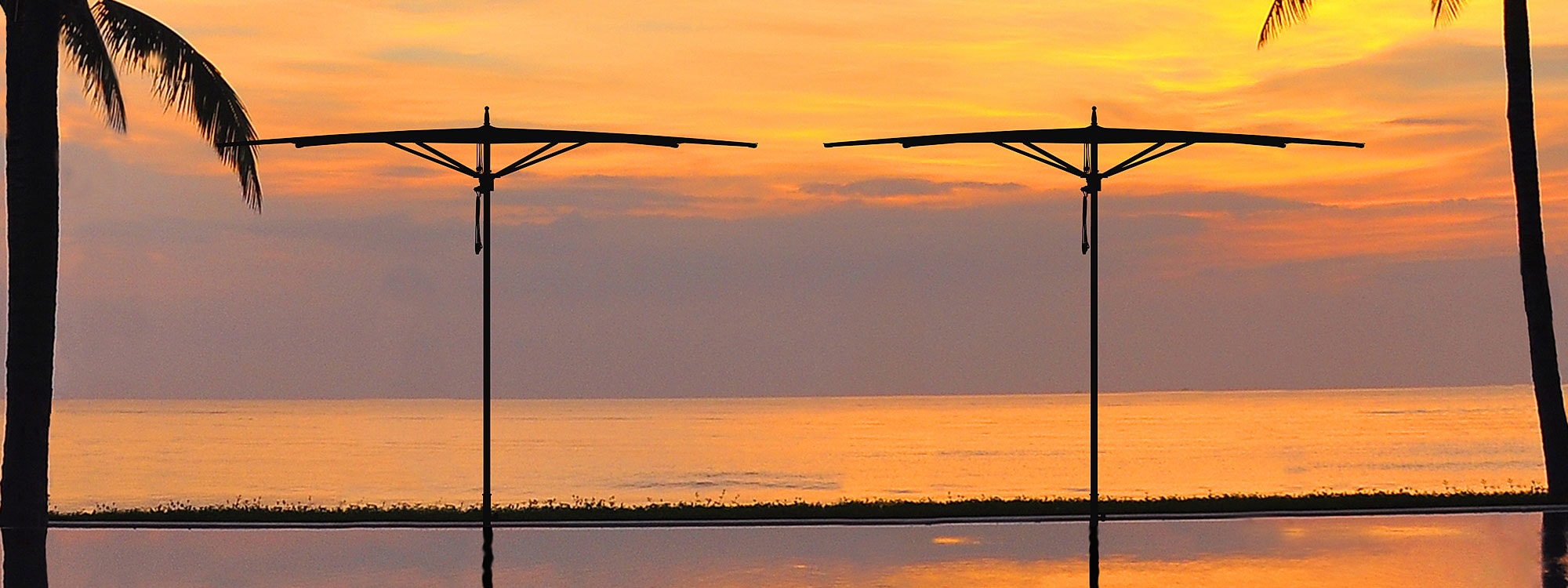 Image of silhouette of pair of Tuuci Ocean Master Zero Horizon parasols at dusk, with beach and sea in background