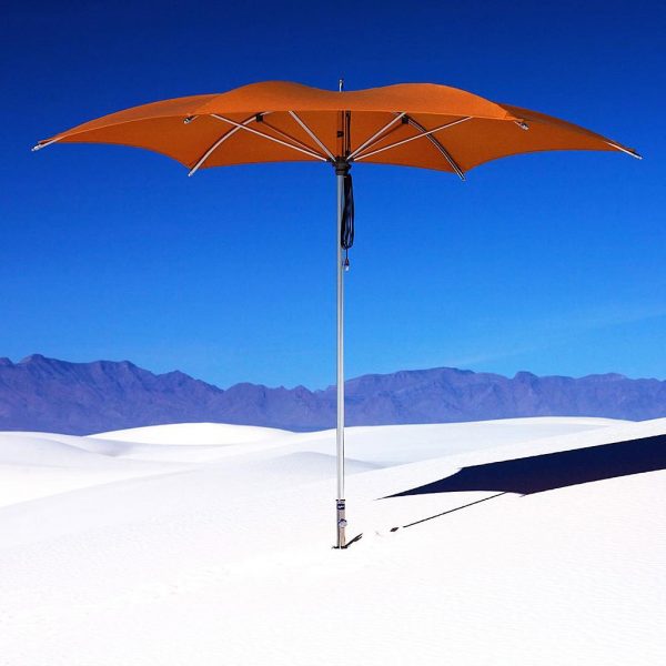 Image of orange Tuuci Crescent parasol mounted in sand with desert and mountains in the background