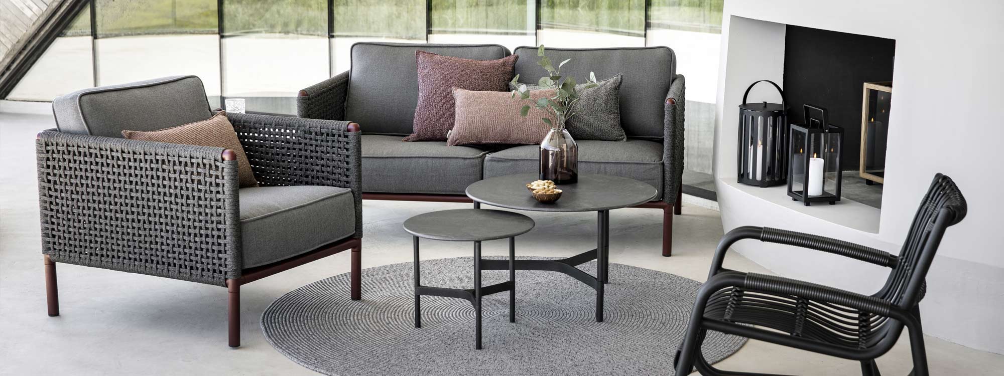 Image of Encore garden sofa and lounge chair with lava-grey Twist coffee tables with black Fossil ceramic tops by Cane-line