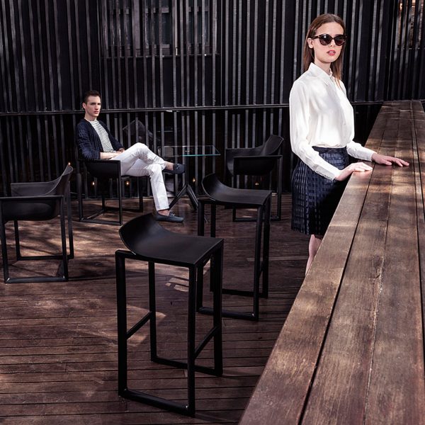 Image of woman stood at wooden planked bar counter with Wall Street modern bar stools and carver chairs by Vondom in the background