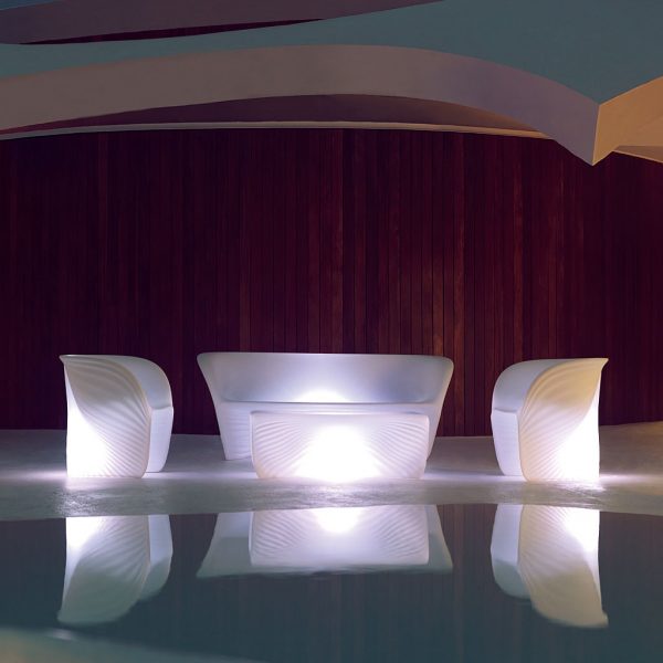 Nighttime image of Vondom Biophilia modernist outdoor lounge furniture with white LED illumination, reflected in water of swimming pool in foreground