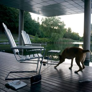 A3 outdoor lounge chair and foot stool in White lacquered oak and galvanised steel on decking next to tranquil Swedish lake.