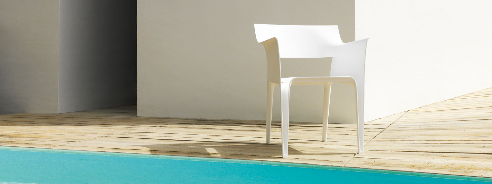 Image of white Vondom Pedrera recycled plastic chair on sunny wooden decking next to swimming pool