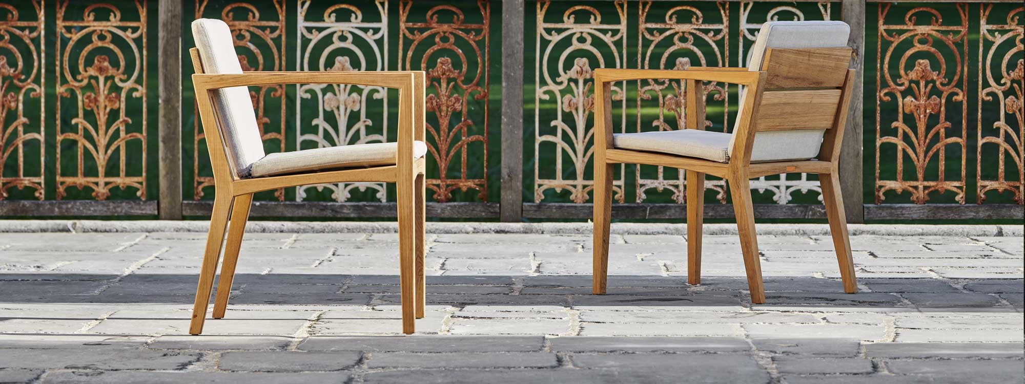 Image of pair of Zenhit teak dining chairs by Royal Botania on terrace in front of rusted steel railings