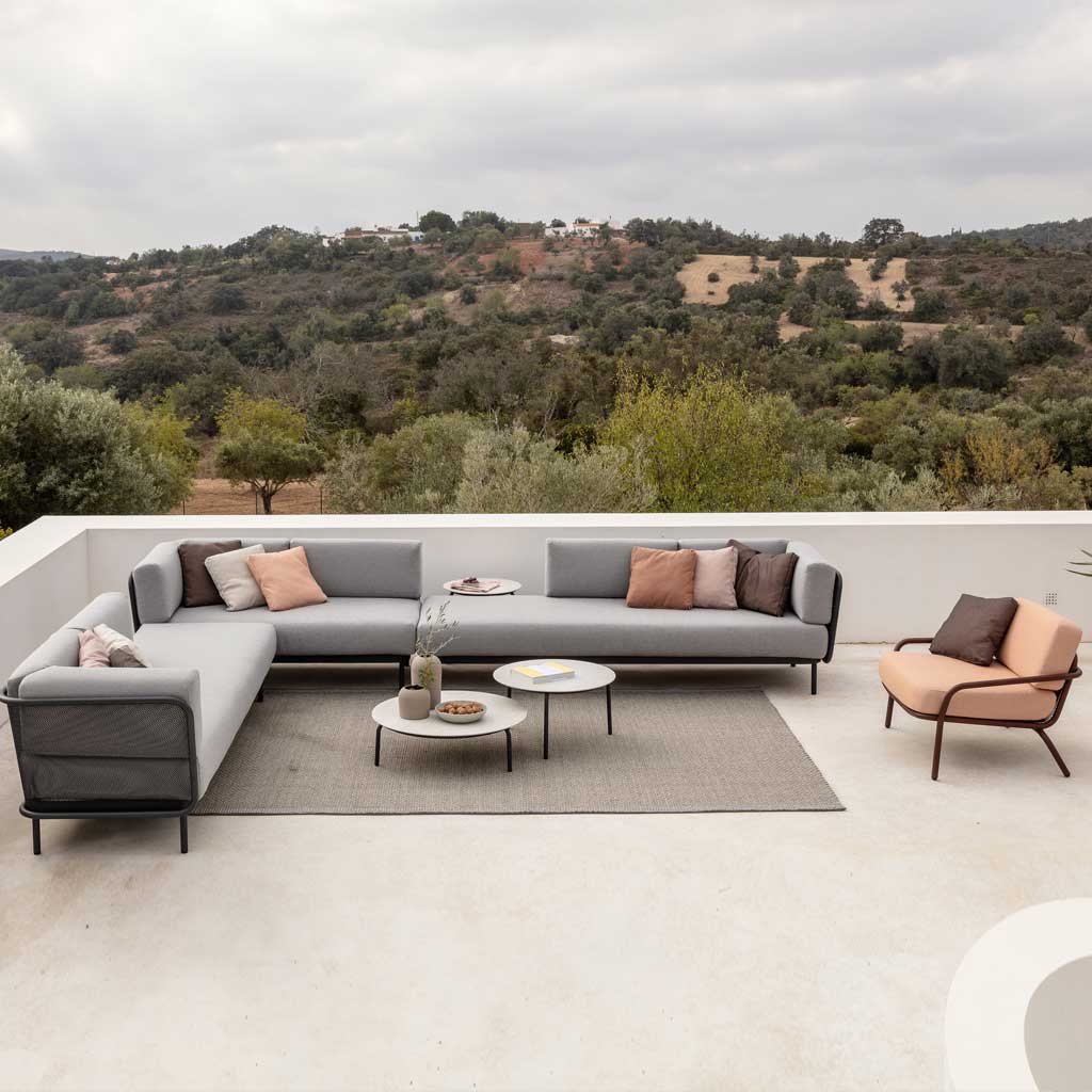 Image of Baza modern garden corner sofa and Starling low tables on terrace with rolling woodland and countryside in background