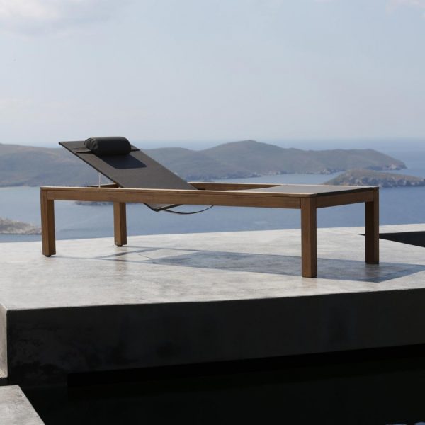 Image of XQI modern teak sun lounger on poured concrete terrace with Aegean sea in background