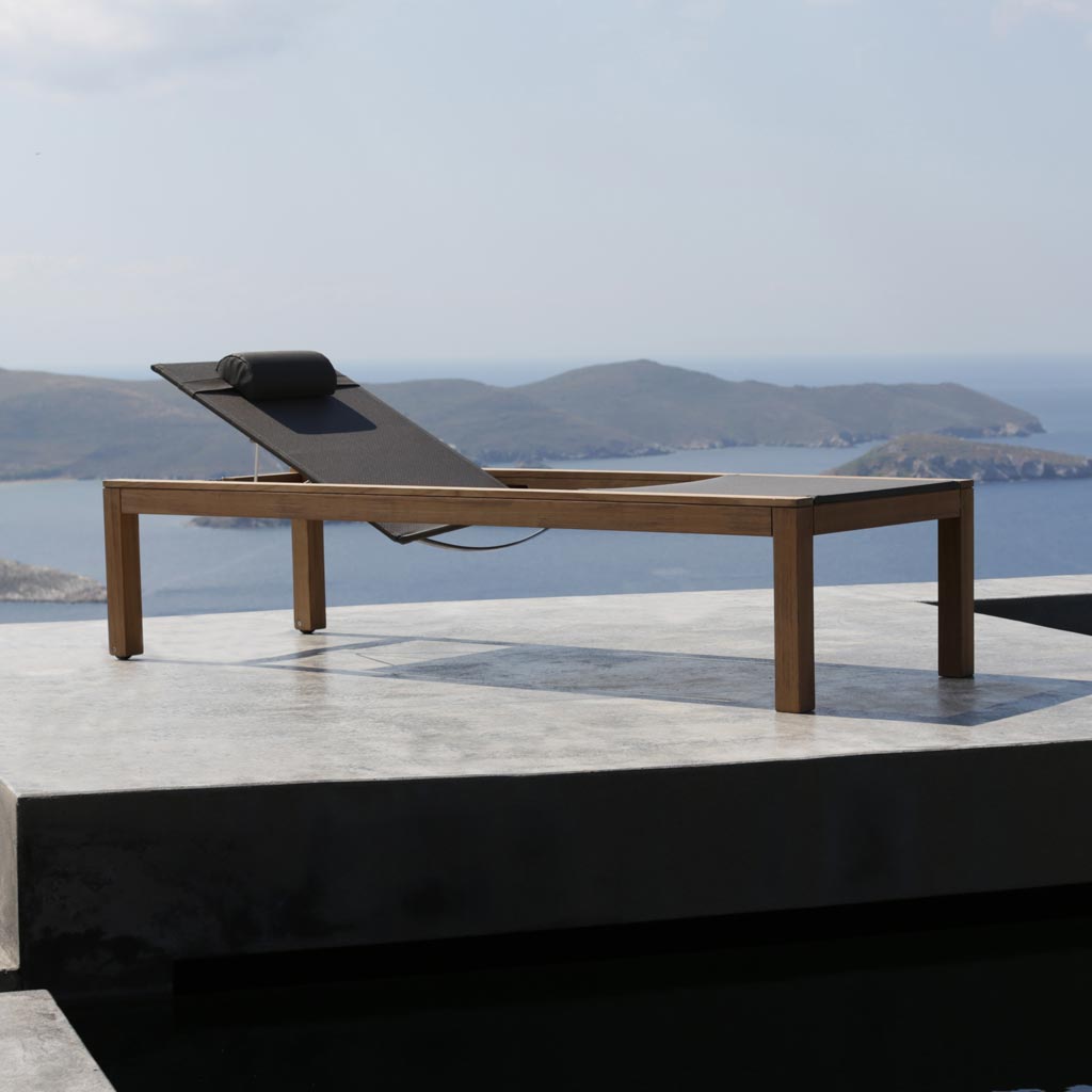 XQI modern teak sun lounger on poured concrete terrace with Aegean sea in background