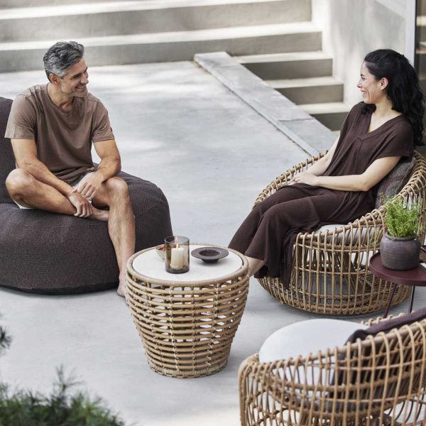Image of couple sat on terrace in Cozy beanbag & Nest lounge chair, with Basket low table by Caneline in the centre