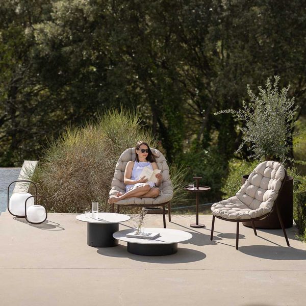 Image of woman sat with feet up on Todus Albus modern outdoor chair, shown on sunny poolside