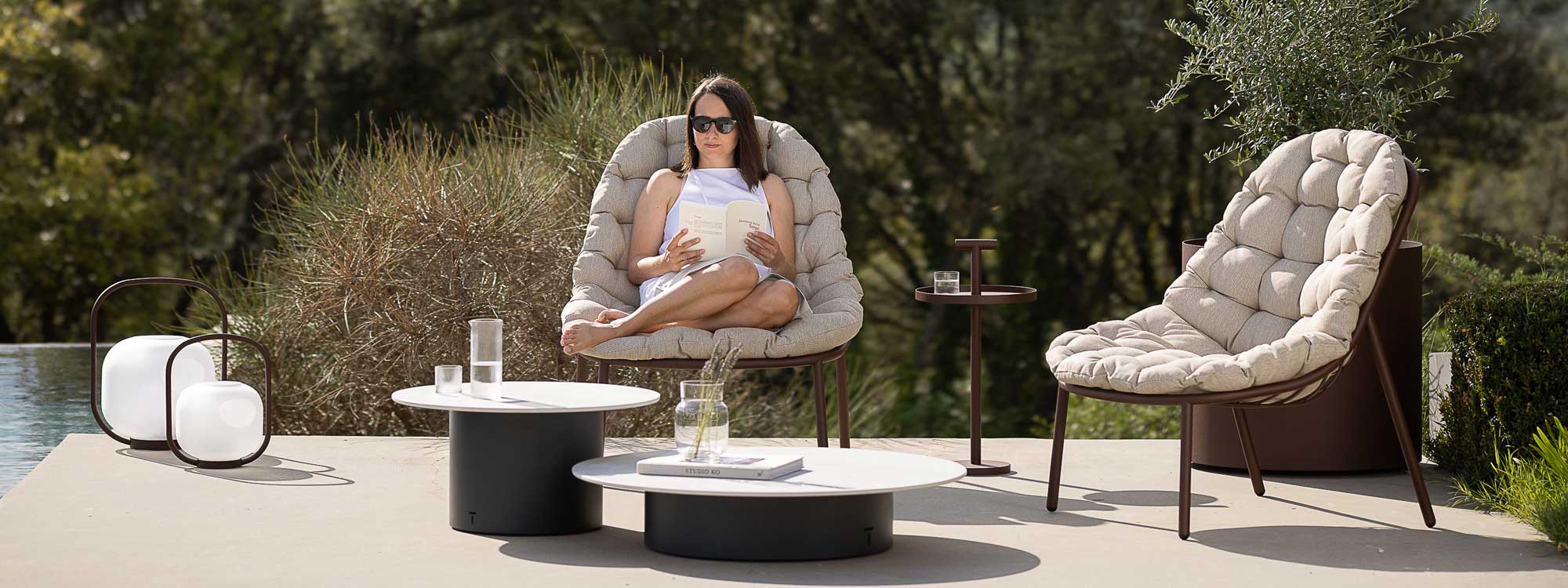 Image of woman sat reading on Todus Albus modern garden chair with Branta low tables in front of her, and Albus low table to one side
