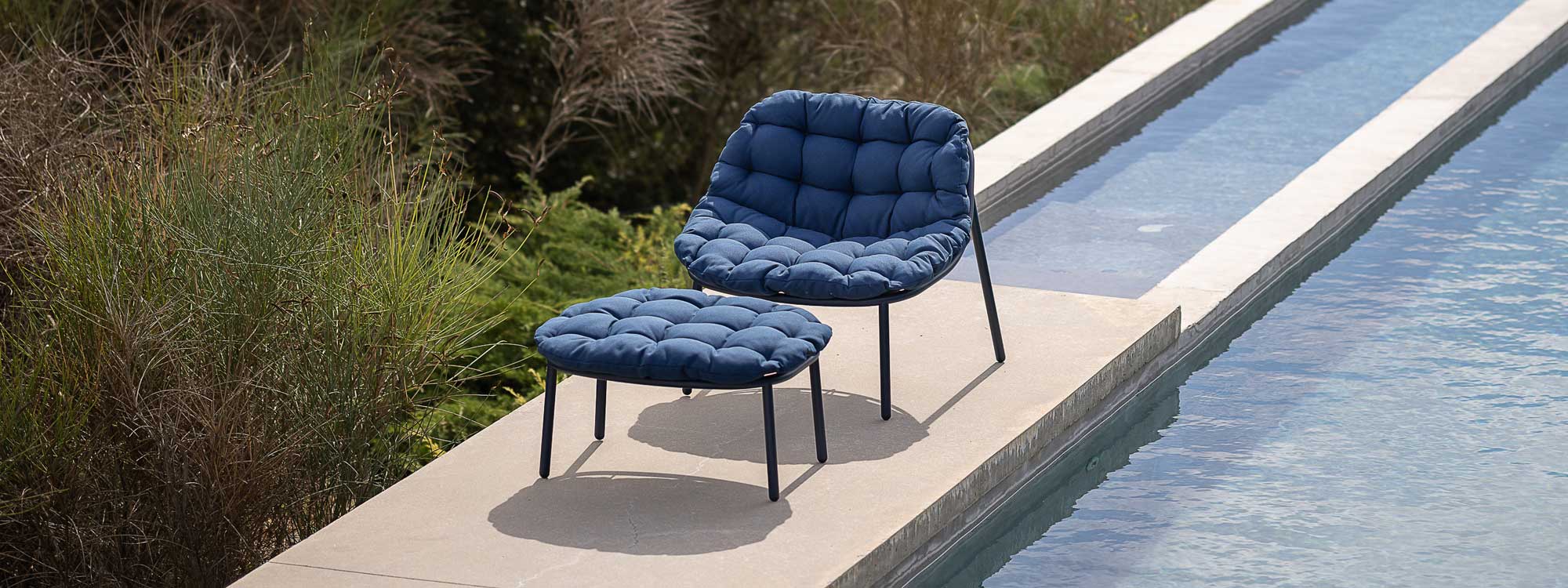 Poolside image of low-backed Albus garden lounge chair and foot stool with blue cushions by Todus