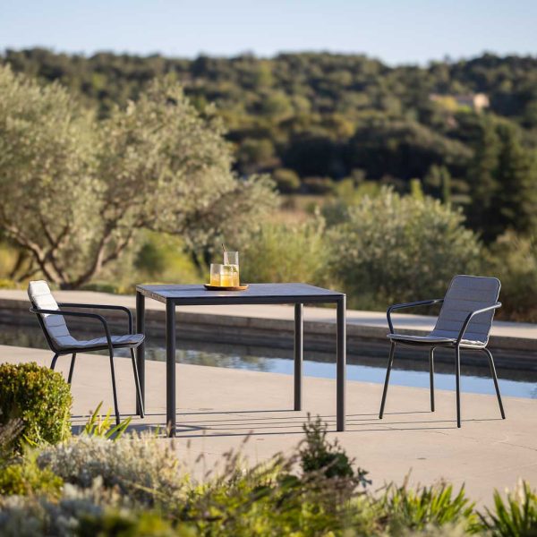 Image of Alca dark grey garden table with Starling modern outdoor chairs on sunny poolside with swimming pool and olive grove in background