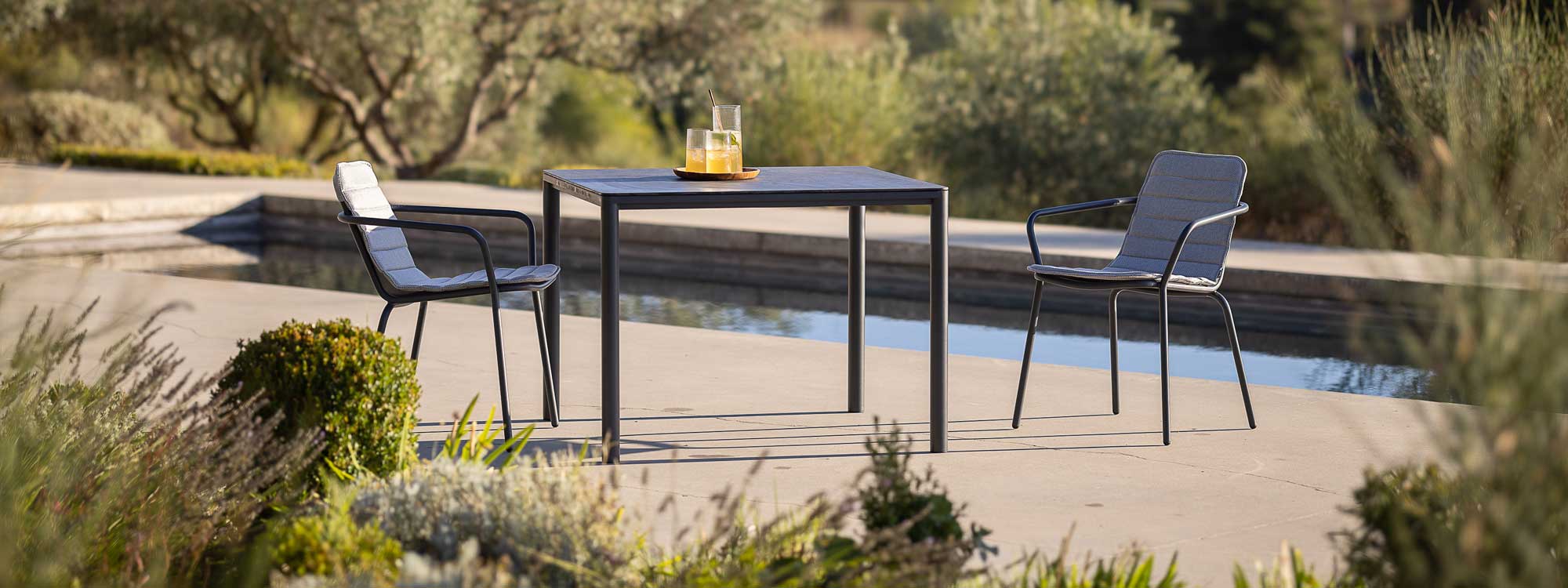 Image of Todus Alca modern garden table and Starling dining chairs with swimming pool and olive trees in the background
