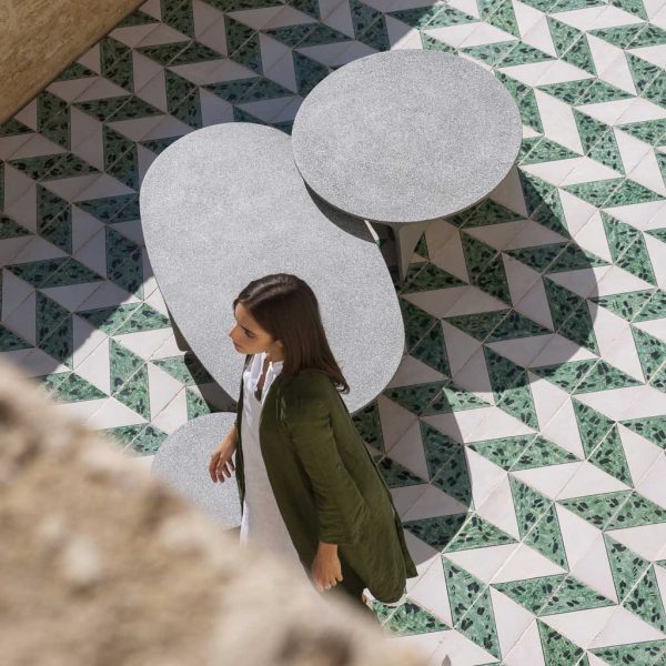 Image of aerial view of woman walking past 2 Aspic concrete low tables by RODA, on green & white tiled courtyard floor