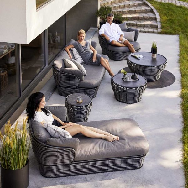 Image of people socializing on black-colored Basket outdoor daybed, sofa .and lounge chair with grey cushions, by Caneline