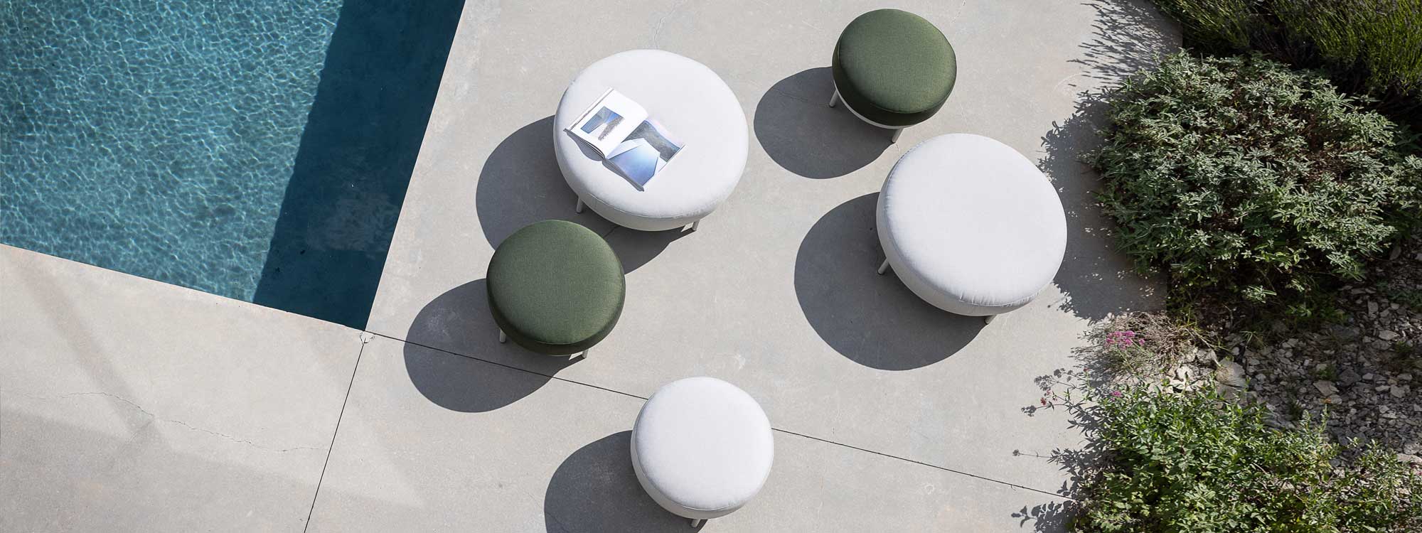 Image of aerial view of different sizes of Baza modern garden poufs with green and white cushions, on sunny poolside
