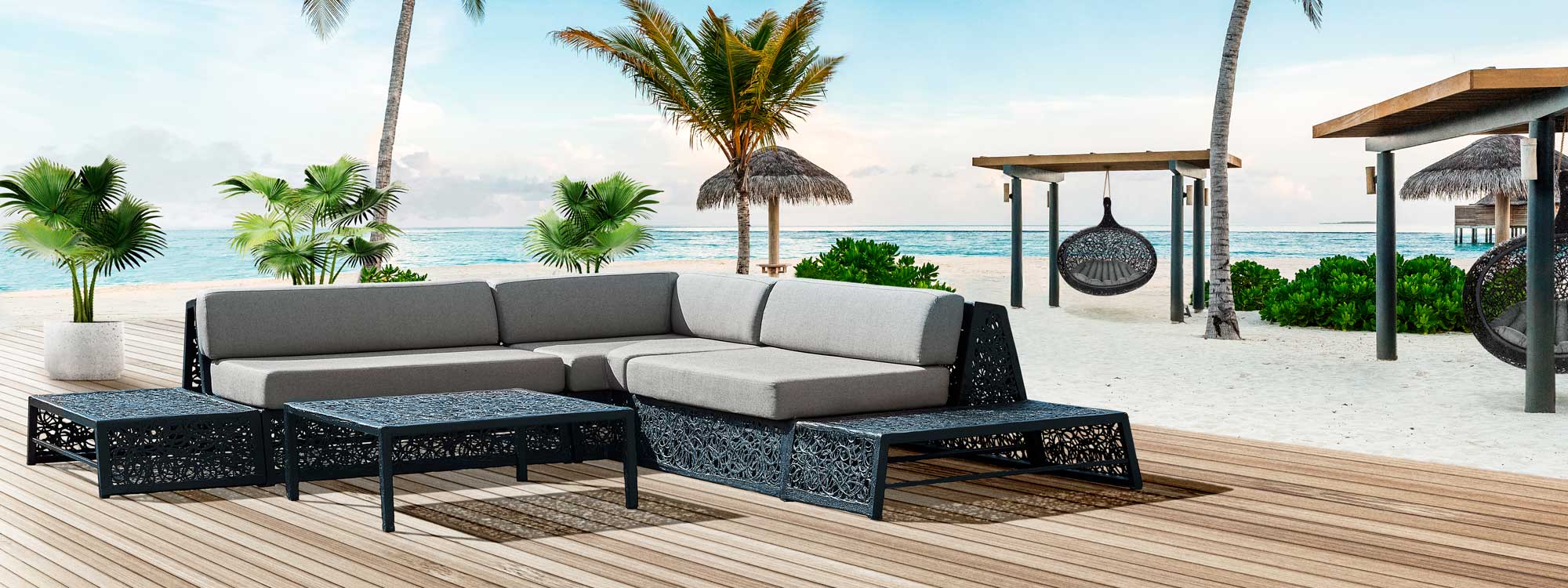 Image of Bios Lounge black sofa with cappuccino cushions on decking, with palm trees, sea and Bios Hide swing seats by Unknown Nordic in the background